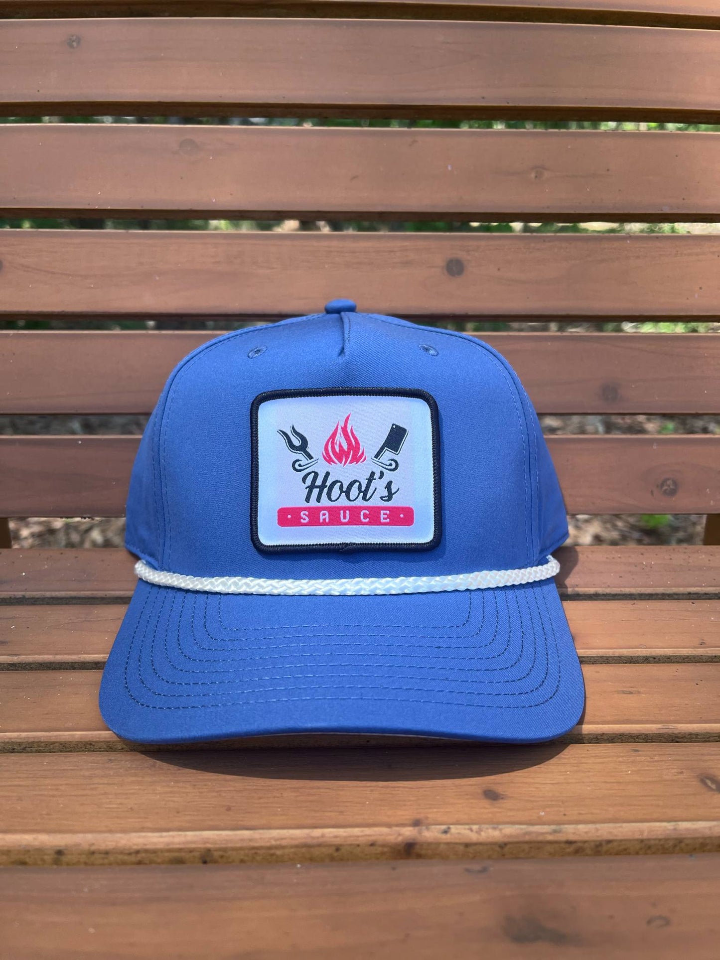 Light blue Hoot’s Sauce rope hat with patch logo on wood bench